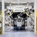 Robôs industriais montam um automóvel em uma fábrica moderna, destacando a automação da linha de produção.