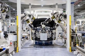 Robôs industriais montam um automóvel em uma fábrica moderna, destacando a automação da linha de produção.