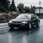 Automóvel Honda preto trafega por uma estrada molhada durante a chuva.