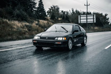 Automóvel Honda preto trafega por uma estrada molhada durante a chuva.