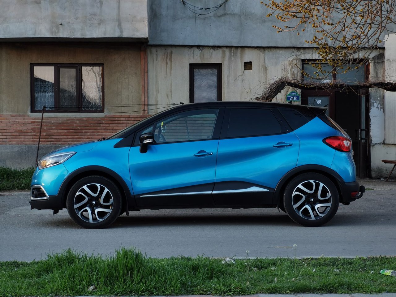 SUV compacto azul estacionado em uma rua urbana, ao lado de um edifício antigo.